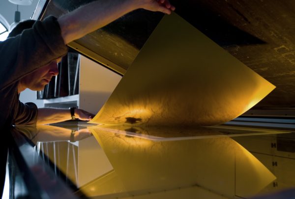 A man placing a transparent film onto of the polymer plate to expose the plate to light